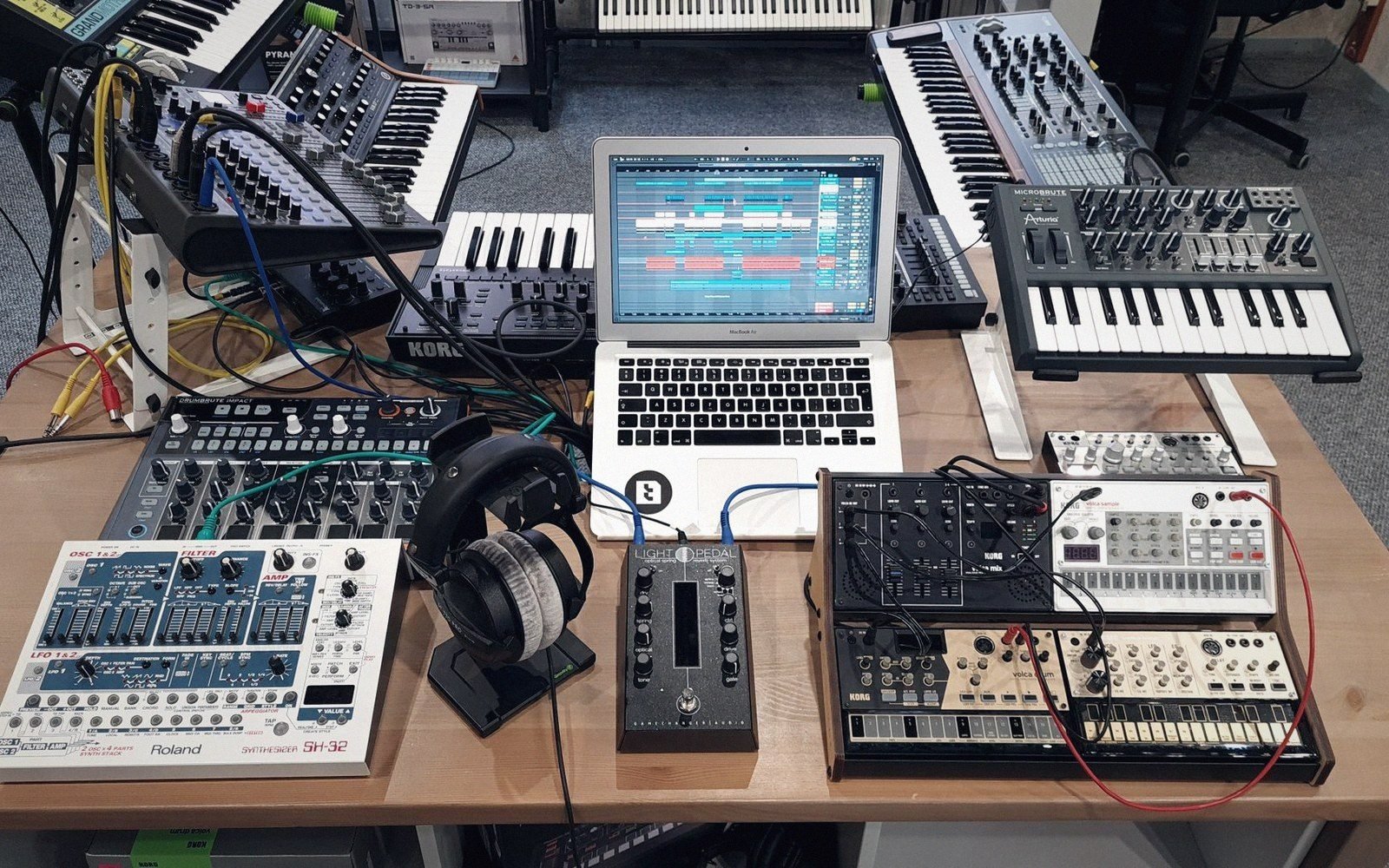 A Roland TB-303 Bass Line synthesiser on a wooden desk, flat-lit from the left, cables coiled at its side