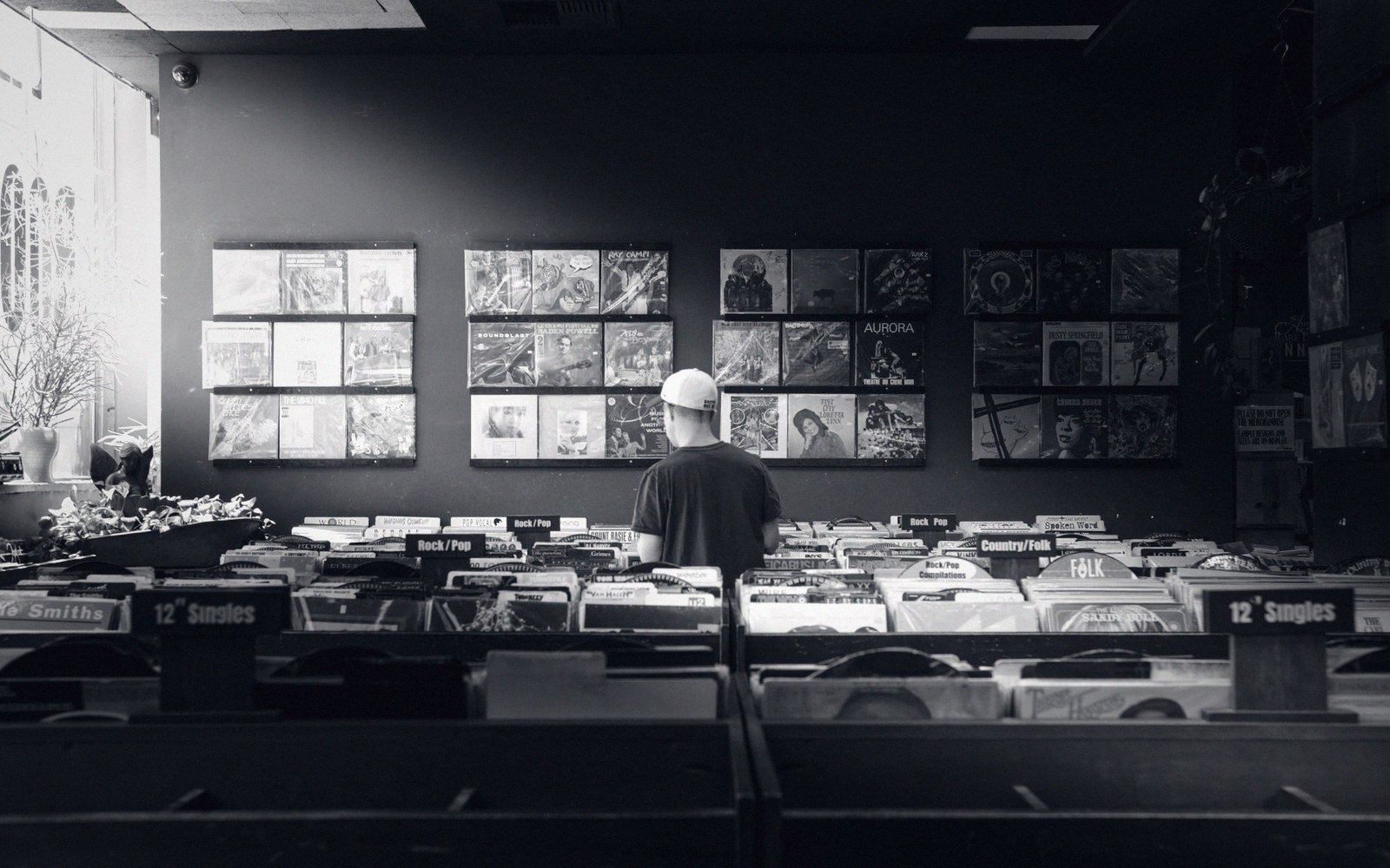 A record-shop browser rack seen from the side, 12-inch sleeves packed spine-out in a wooden divider rack